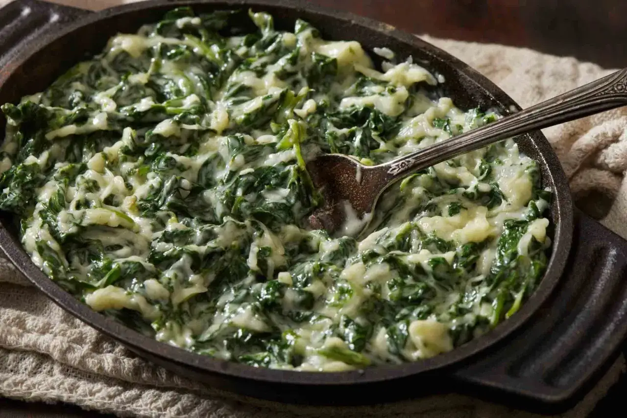 Cremosas espinacas a la crema, servidas en una sartén de hierro fundido con una cuchara lista para servir.