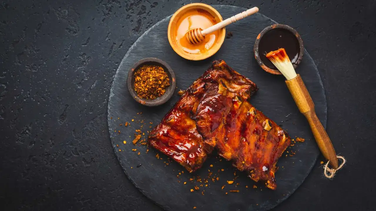 Costillas al horno glaseadas con miel y salsa barbacoa, acompa&ntilde;adas de especias y un pincel para untar.