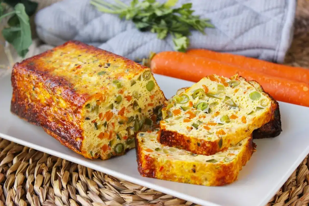 Un delicioso quiche de verduras, con trozos de zanahoria y guisantes, servido en una bandeja blanca.