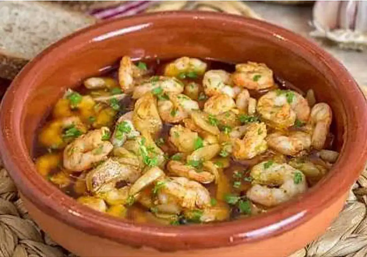 Gambas al ajillo burbujeantes en cazuela de barro, con perejil picado y pan rústico al fondo.