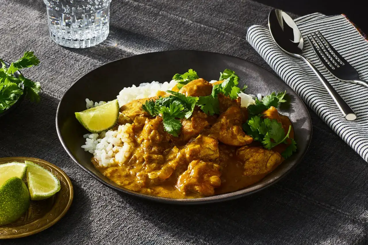 Delicioso pollo al curry con arroz blanco, cilantro fresco y gajos de lima. Un plato reconfortante listo para disfrutar.