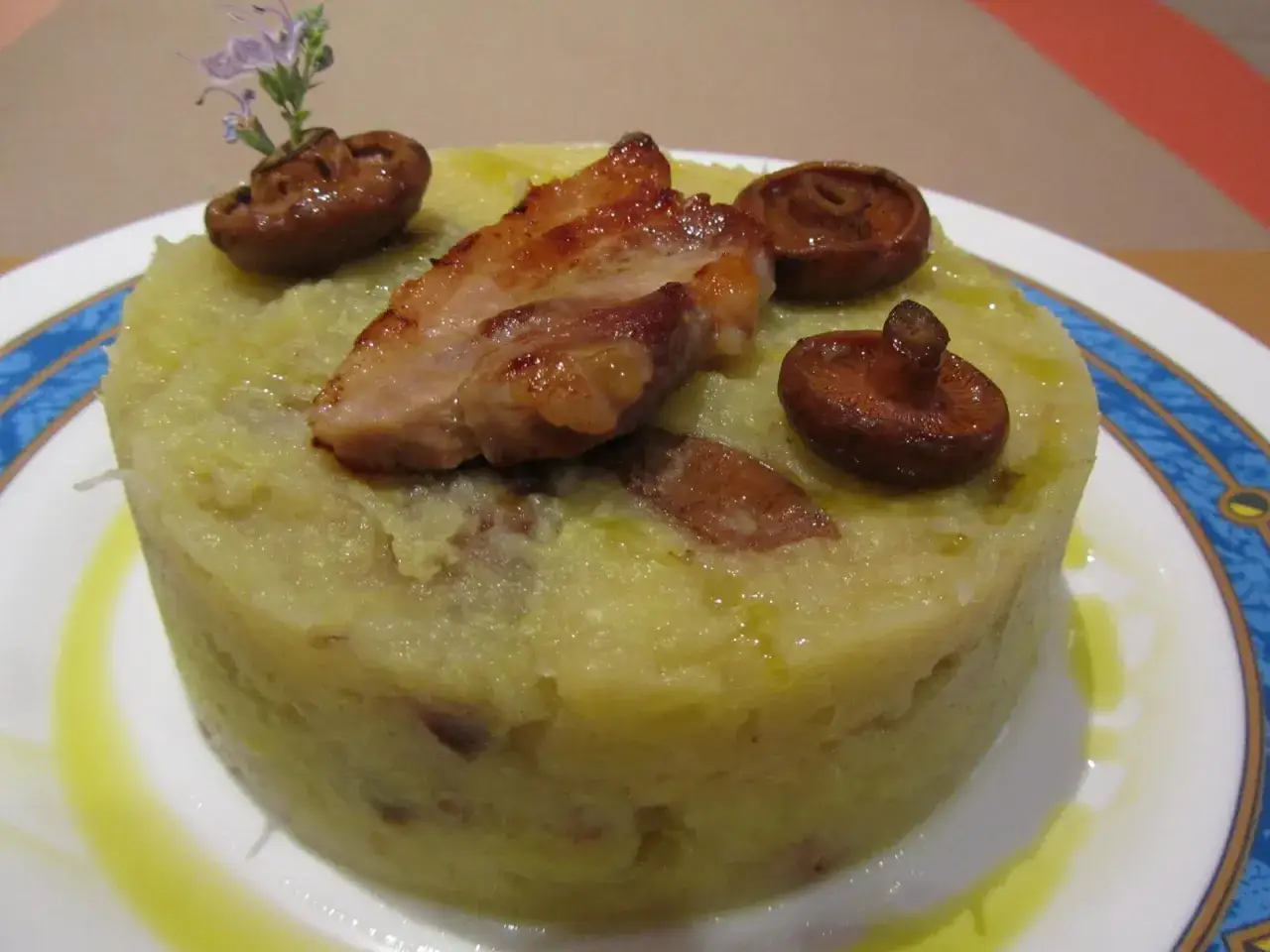 Delicioso trinxat de la Cerdanya con trozos de panceta crujiente y setas, decorado con una flor.