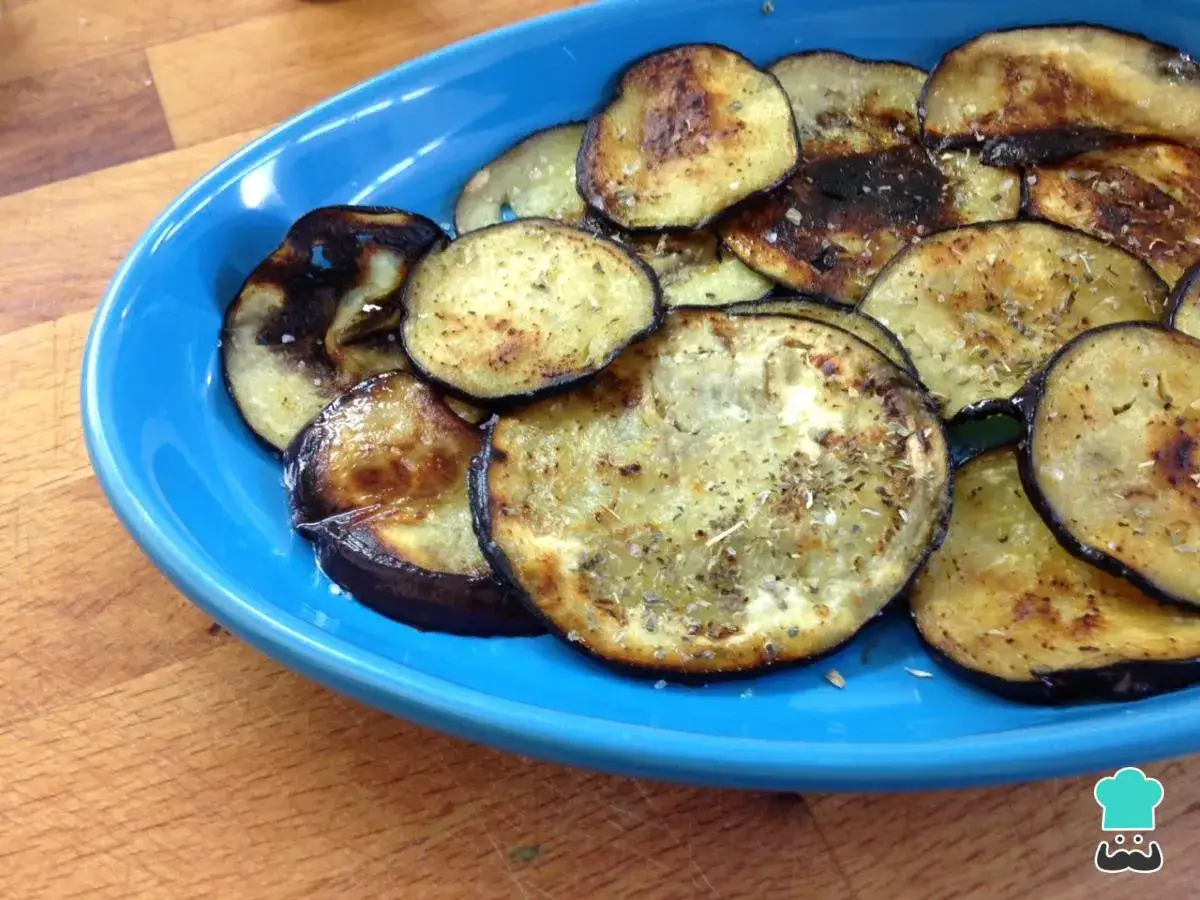 Berenjenas a la plancha, doradas y sazonadas con hierbas, servidas en un plato azul.