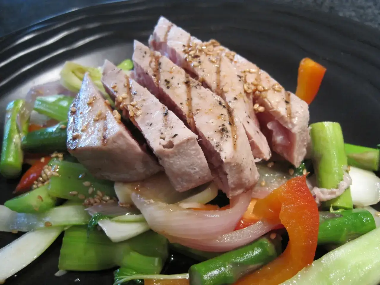 Atún a la plancha en rodajas, servido sobre verduras salteadas con pimientos y cebolla.