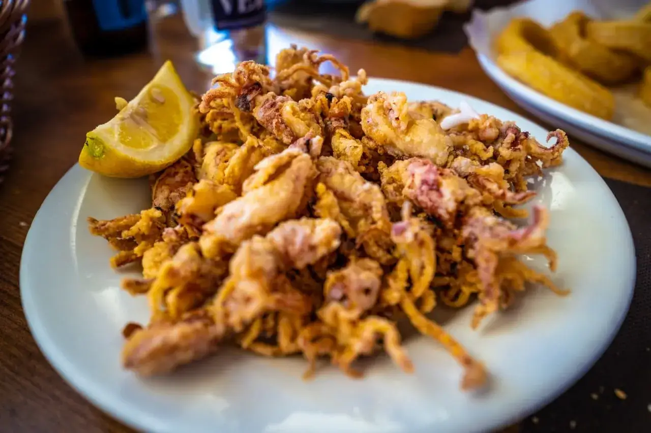 Plato de puntillas de calamar fritas, crujientes y doradas, servido con una rodaja de lim&oacute;n.