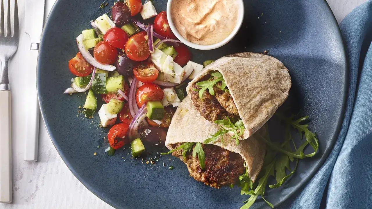 Deliciosa hamburguesa de lentejas en pan de pita, acompa&ntilde;ada de ensalada griega y salsa.