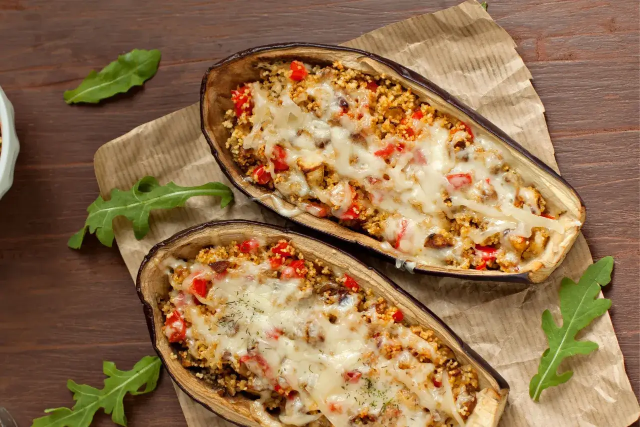 Dos mitades de berenjenas rellenas con cuscús, pimientos y queso derretido, cocinadas en freidora de aire.