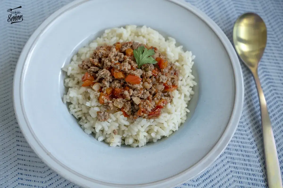 Plato de arroz blanco cubierto con una generosa porci&oacute;n de arroz con carne picada, adornado con una hoja de perejil.