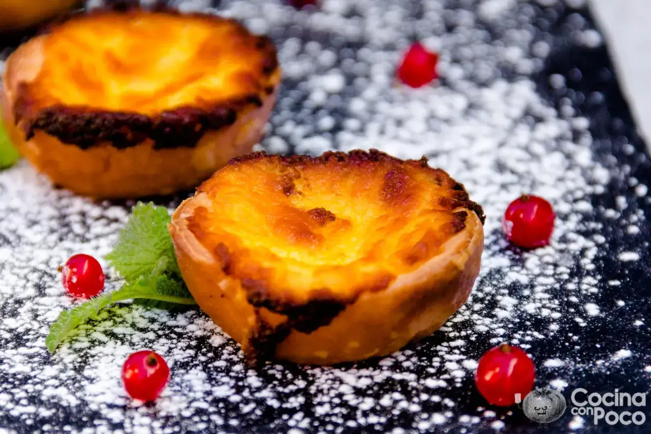 Pastelitos de Bel&eacute;m dorados y cremosos, espolvoreados con az&uacute;car glas y decorados con frutos rojos.