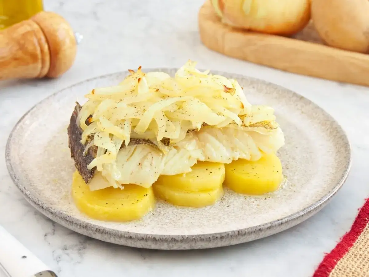 Delicioso bacalao a la portuguesa, servido sobre patatas y cubierto con cebolla caramelizada.