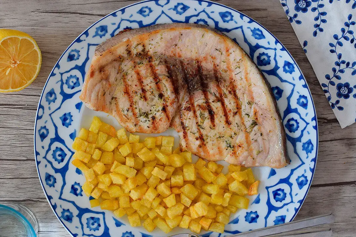 Un jugoso emperador a la plancha con patatas fritas crujientes, servido en un plato decorado con motivos azules.