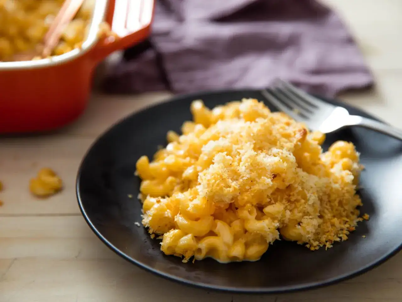 Mac and cheese cremoso con cobertura crujiente de pan rallado, servido en un plato negro con un tenedor.