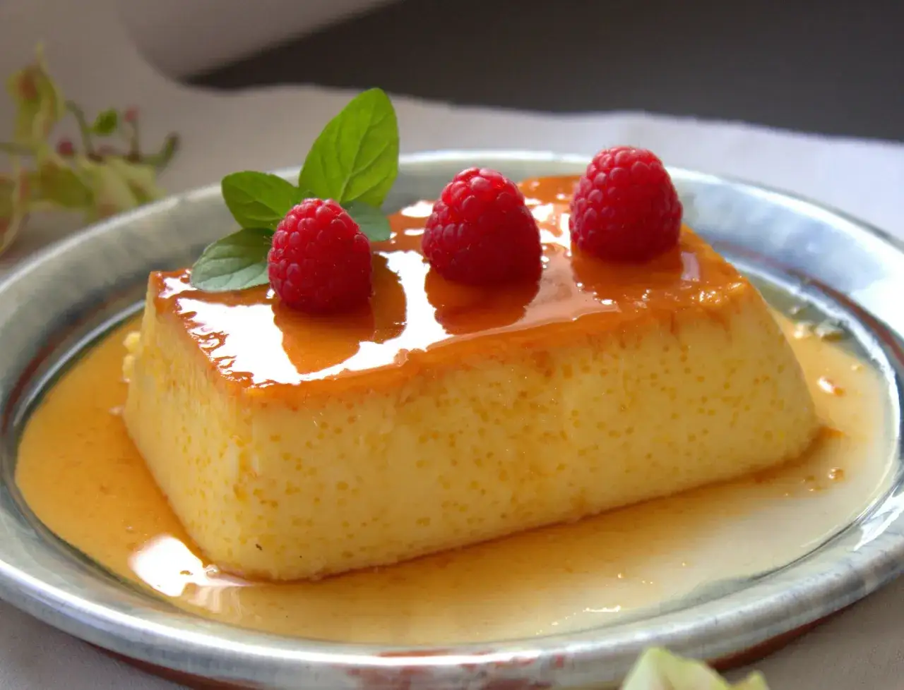 Delicioso flan de queso Philadelphia bañado en caramelo, decorado con frambuesas y menta fresca.