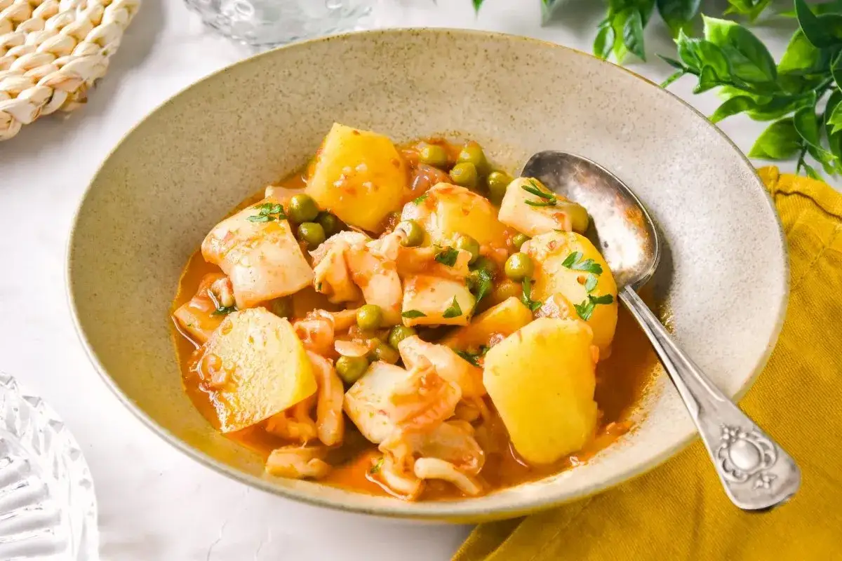 Un tazón de sepia con patatas, guisantes y perejil picado en una salsa rojiza. Un plato reconfortante y sabroso.