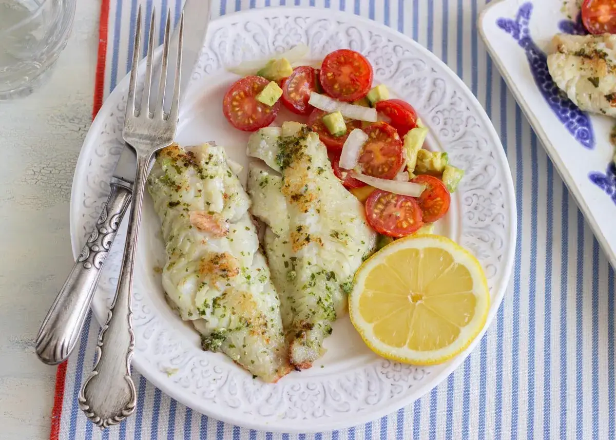 Deliciosa gallineta a la plancha con ensalada de tomate y aguacate, servida con una rodaja de lim&oacute;n.