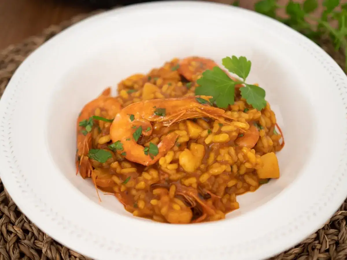 Un plato de arroz con gambas, decorado con perejil fresco. El arroz tiene un color dorado intenso y se aprecian trozos de marisco.
