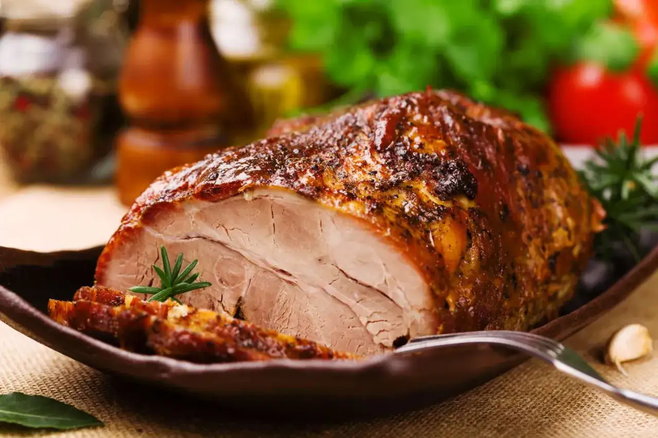 Un jugoso lomo de cerdo al horno, dorado y tierno, servido en plato de barro con romero y ajo.