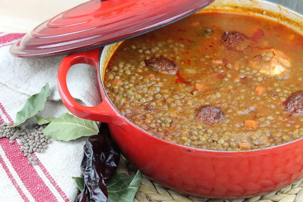 Olla roja con lentejas con chorizo, zanahoria y laurel. Un plato reconfortante listo para servir.