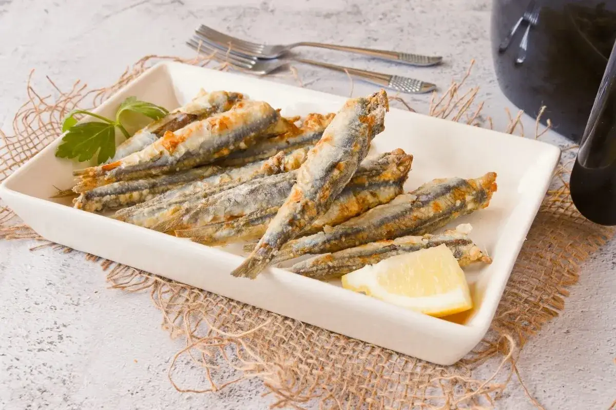 Boquerones crujientes en freidora de aire, servidos en plato blanco con lim&oacute;n y perejil.