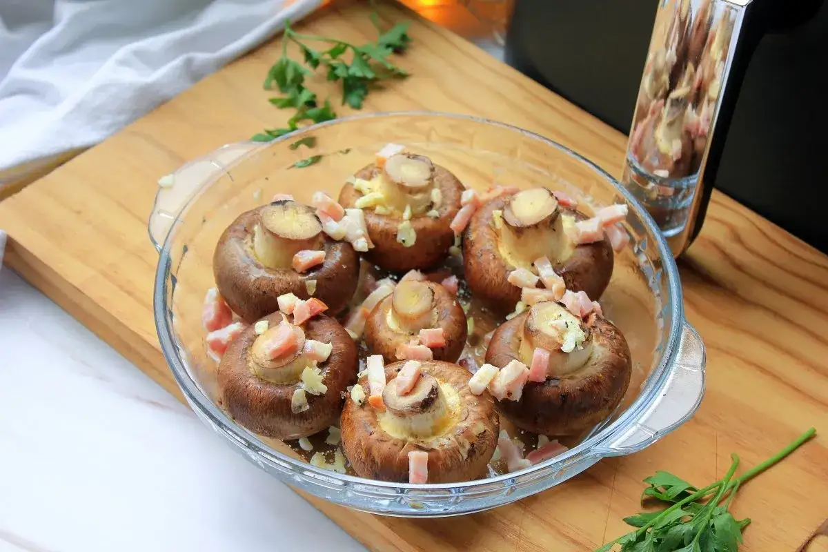 Champiñones rellenos listos para la freidora de aire. Cubiertos con trocitos de tocino y queso.