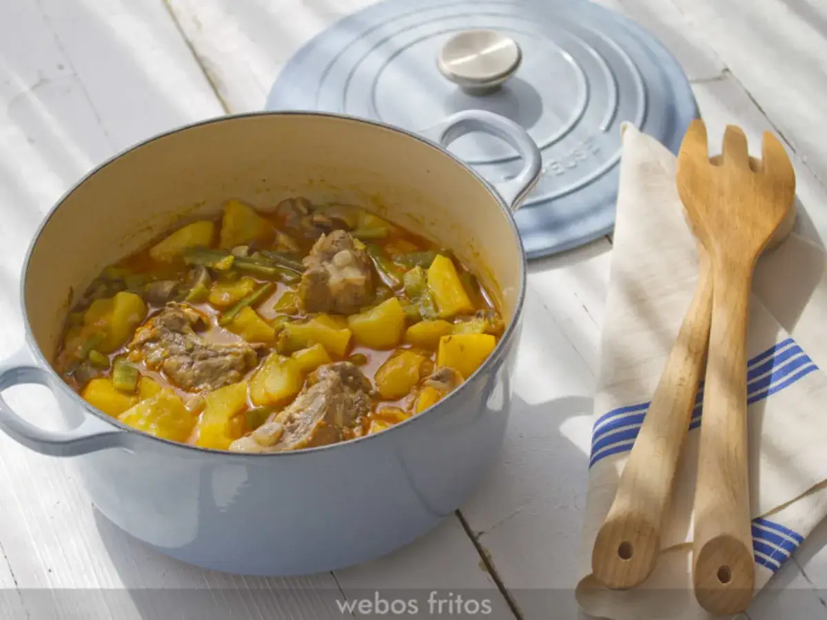 Costillas guisadas de la abuela en una olla azul, con patatas, jud&iacute;as verdes y champi&ntilde;ones. Servido con utensilios de madera.