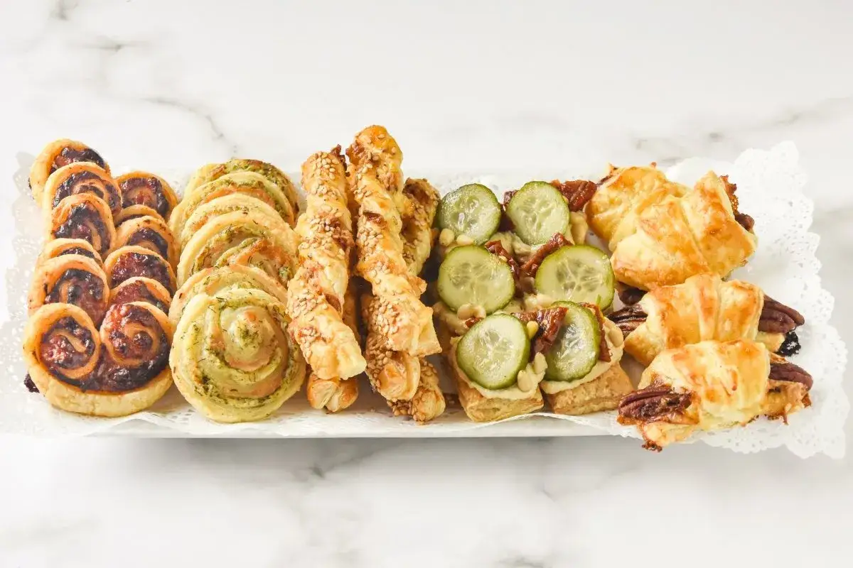 Bandeja con variedad de bocadillos salados y dulces, perfectos para tus recetas con hojaldre: palmeritas, rollitos de pesto, palitos de s&eacute;samo, canap&eacute;s de pepino y solomillo.