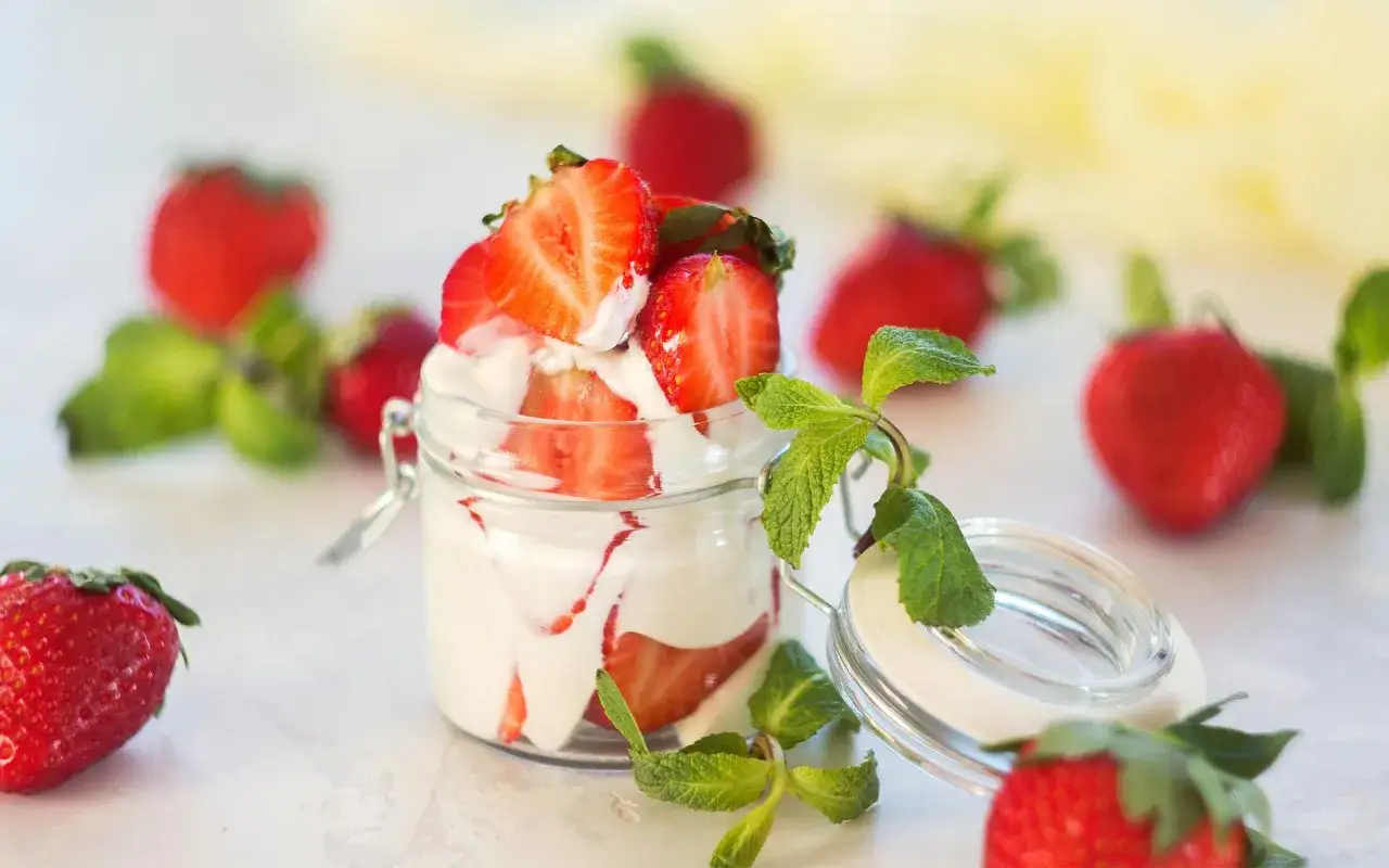 Delicioso mousse de yogur con fresas frescas y hojas de menta en un frasco de vidrio.