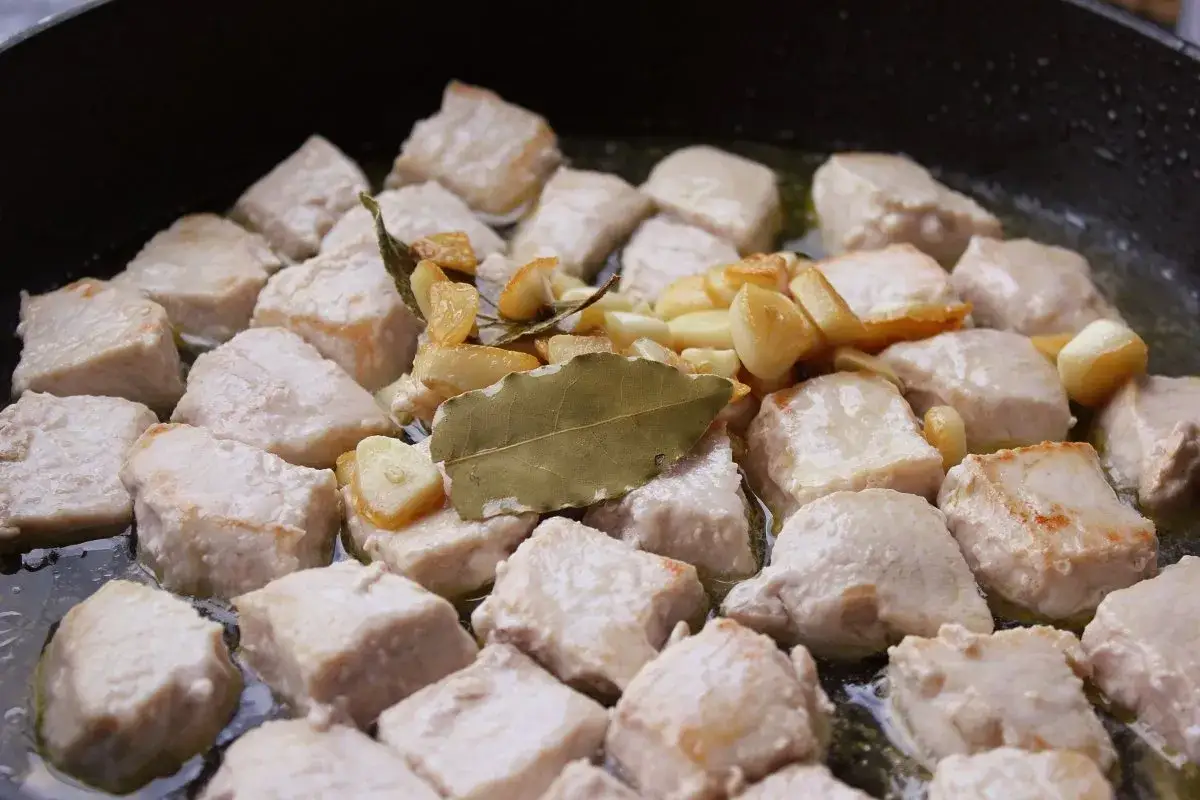 Sabrosa carne al ajillo cocinándose en una sartén con ajo laminado y hojas de laurel.