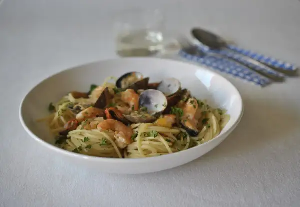 Un plato de spaghetti frutti di mare con gambas, mejillones y almejas, adornado con perejil fresco.