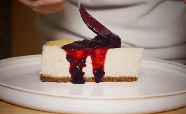 Un trozo de new york cheesecake cremoso con salsa de frutos rojos cayendo.
