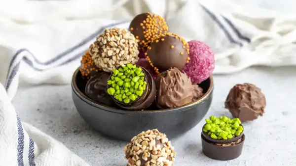 Un tazón lleno de deliciosas trufas de chocolate, algunas cubiertas de frutos secos, otras con chispas de colores y pistachos.