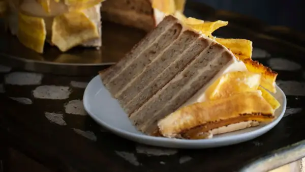 Rebanada de tarta de plátano con capas de bizcocho y crema, decorada con trozos de plátano caramelizado.