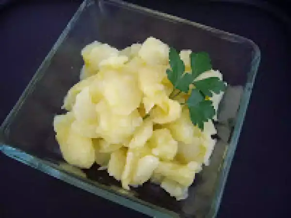 Un cuenco de cristal contiene patatas al montón, un plato sencillo y reconfortante, adornado con una ramita de perejil fresco.