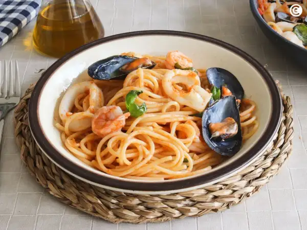Un plato de espaguetis a la marinera con gambas, calamares y mejillones, servido en un cuenco sobre una esterilla de mimbre.