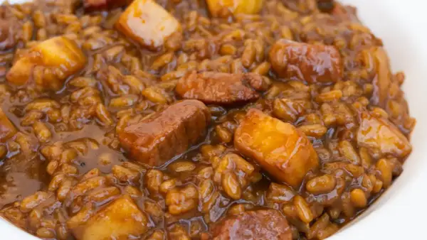 Un plato de arroz con acelgas y trozos de carne en una salsa oscura y apetitosa.