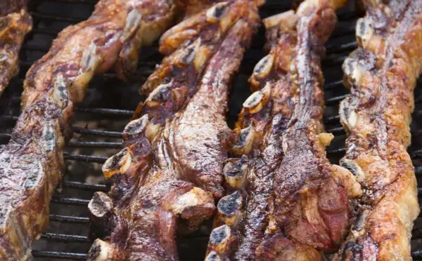 Costillas de churrasco a la plancha, doradas y jugosas, cocinándose lentamente sobre la parrilla.