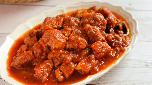 Magro con tomate en un plato blanco, con trozos de carne en salsa roja.