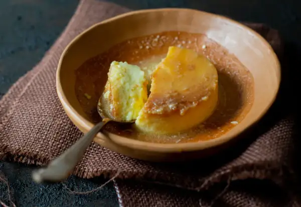 Un trozo de flan de yogur cremoso, bañado en caramelo líquido, servido en un cuenco de barro.