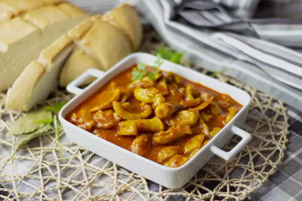 Deliciosa jibia en salsa, servida en un cuenco blanco, acompañada de pan rústico y hojas de laurel.