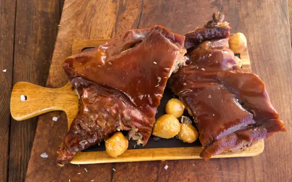 Delicioso cochinillo al horno, crujiente y jugoso, servido con patatas asadas.