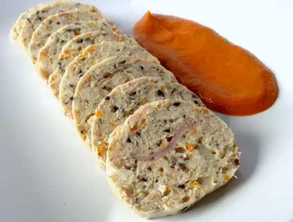Fiambre de pollo casero en rodajas, con trocitos de verdura y jamón, acompañado de una salsa naranja.