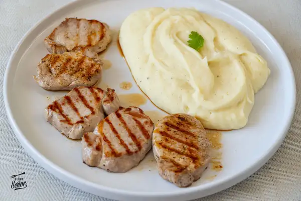 Cinco medallones de solomillo a la parrilla con puré de patatas cremoso, decorado con una ramita de perejil.