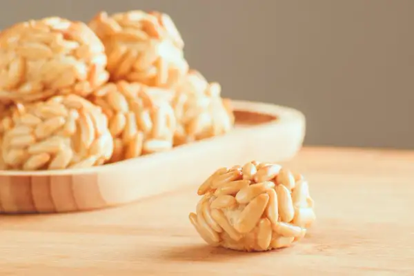 Rosquillas de naranja cubiertas de piñones, con un dulce aroma cítrico y un crujiente exterior.