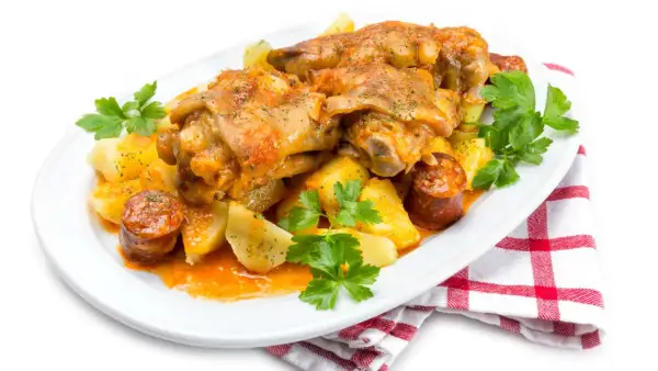 Manitas de cerdo receta tradicional de la abuela, con patatas y chorizo, servido en plato blanco con perejil fresco.