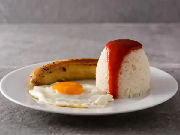Un plato de arroz a la cubana con huevo frito y salchicha, cubierto con salsa de tomate.