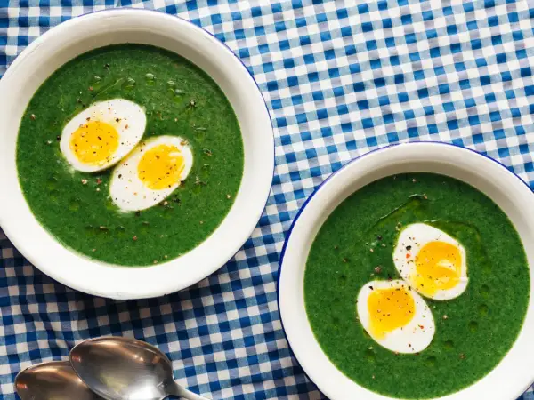 Dos cuencos de espinacas a la crema con huevos duros cortados por la mitad, servidos sobre un mantel de cuadros azules y blancos.
