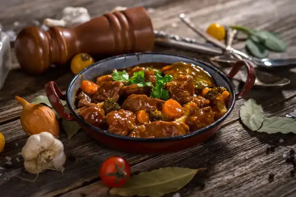Caldereta de cordero humeante, con trozos de carne tierna, zanahoria y brócoli, servida en una cazuela rústica.