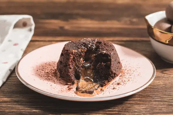 Coulant de chocolate con centro líquido y cremoso, espolvoreado con cacao en polvo sobre un plato rosa.