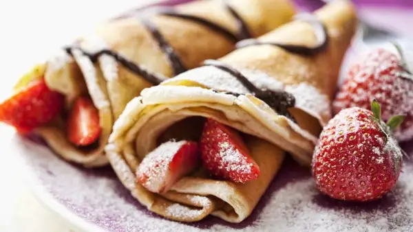 Deliciosos crepes sin huevo rellenos de fresas y bañados en chocolate, espolvoreados con azúcar glas.