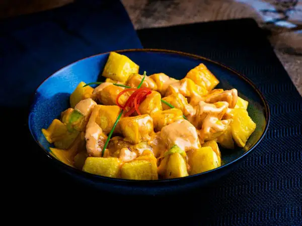 Patatas bravas receta: trozos dorados de patata cubiertos con una cremosa salsa rosada y decorados con pimiento rojo y cebollino.